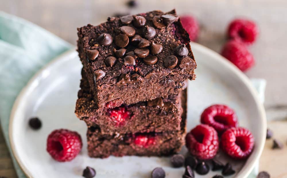 Stacked brownies on plate with chocolate chips and raspberries